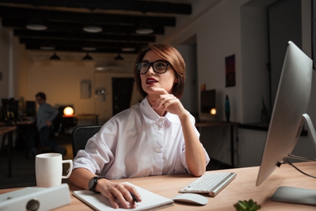 Happy pensive young businesswoman in glasses thinking and working in office