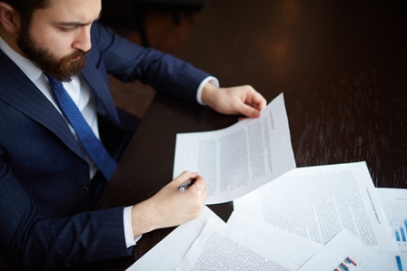 Image of serious businessman signing contract at workplace