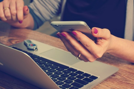 Email Control - Woman working at laptop-holding smartphone